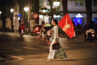 Như bao người hâm mộ,sau chiến thắng của Việt nam trước Campuchia tại giải bóng đá AFF CUP, tôi cùng bạn bè hòa vào dòng người trên phố để đón mừng chiến thắng. Trong một khoảnh khắc bất chợt, tôi bất ngờ thấy hình ảnh một người phụ nữ hiên ngang đi qua phố với lá cờ trên vai. Không bỏ lỡ khoảnh khắc này tôi đã kịp thời lưu lại được chỉ trong giây phút ,với thần thái và vẻ mặt rạng ngời phấn chấn của người phụ nữ trong tà áo dài truyền thống đón mừng chiến thắng của đội tuyển VN. Người mà sau này tôi mới biết là nghệ sĩ Chiều Xuân.Theo cá nhân tôi bức hình này thật sự chứa đầy cảm xúc, nhân vật có phong thái nhẹ nhàng nhưng tràn đầy niềm tin vào chiến thắng.